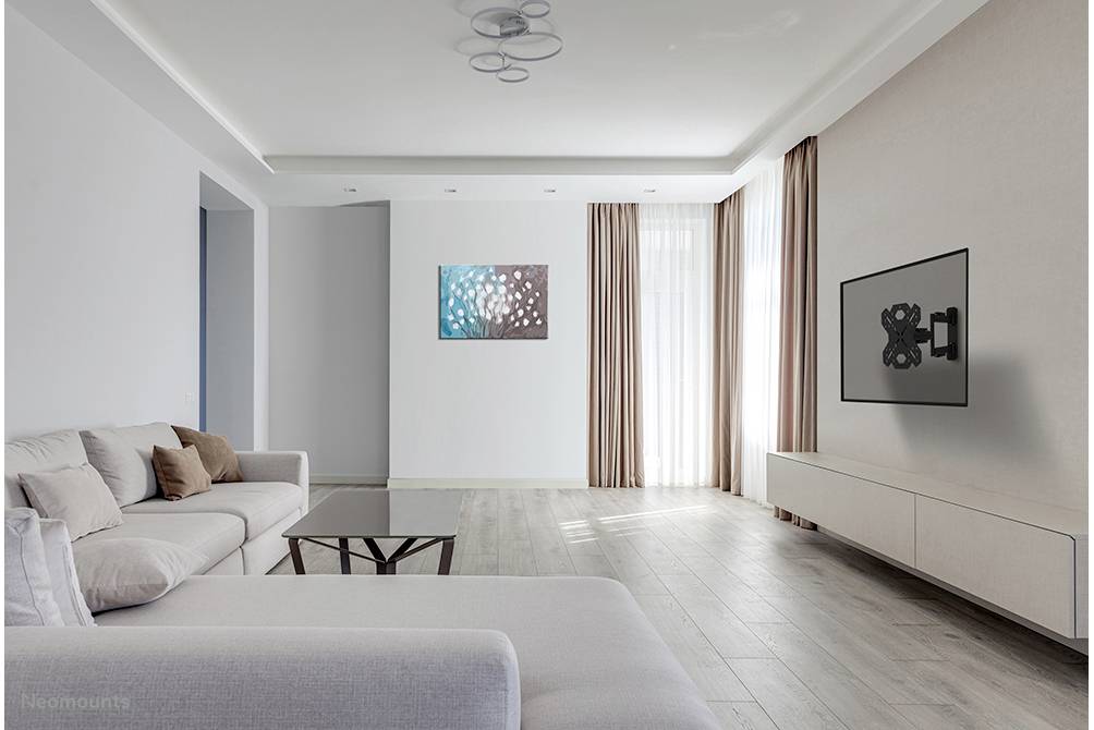 Helles Wohnzimmer mit weißen Wänden, grauem Sofa, Couchtisch und einem Wandbild links. Rechts steht ein TV auf einem flachen TV-Möbel.