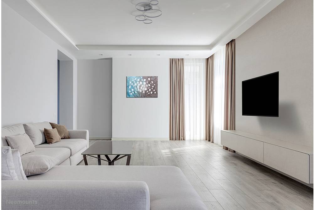 Helles, minimalistisches Wohnzimmer mit einem grauen Sofa, einem niedrigen Tisch und einem an der Wand montierten Flachbildfernseher.