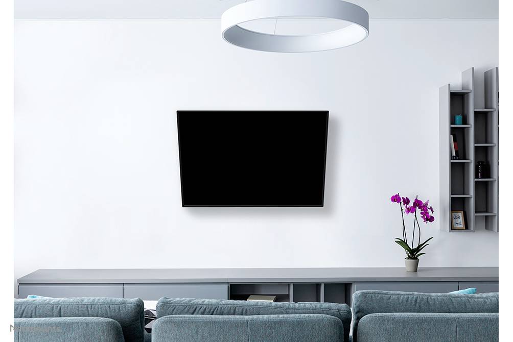 Ein modernes Wohnzimmer mit einem an der Wand montierten Fernseher, einem blauen Sofa und einem Regal mit lila Orchidee.