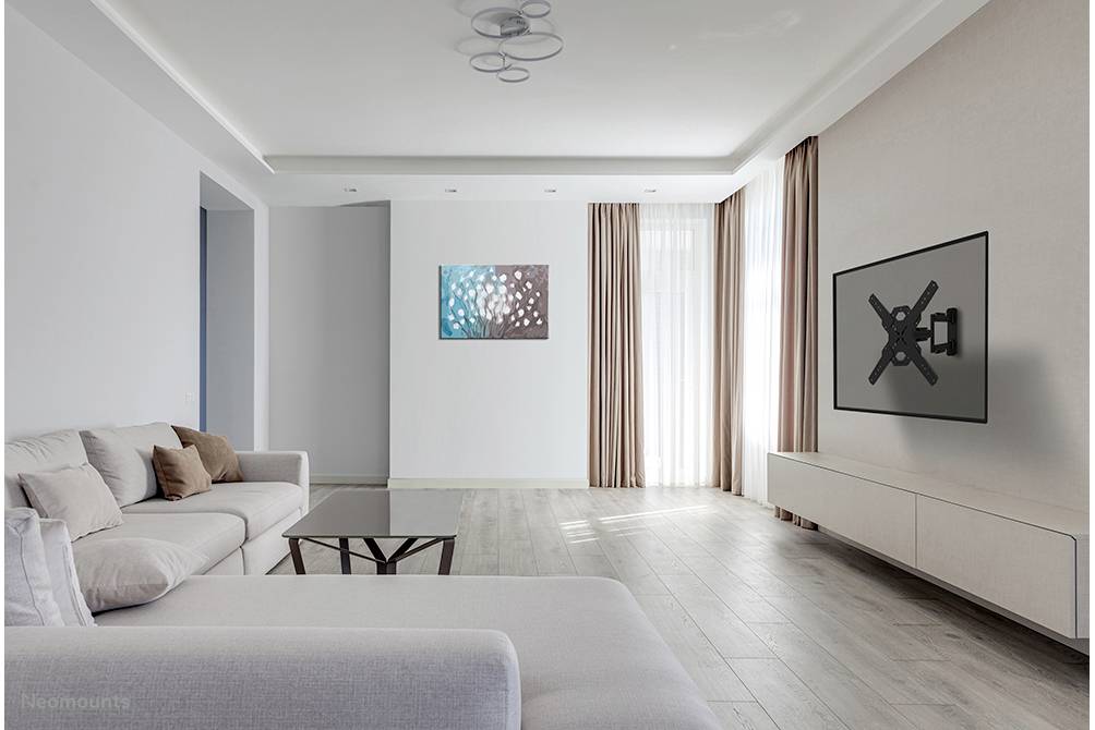 Modernes Wohnzimmer mit grauem Sofa, Couchtisch und Wandhalterung ohne TV. Ein Gemälde und lange Vorhänge zieren die Wände.