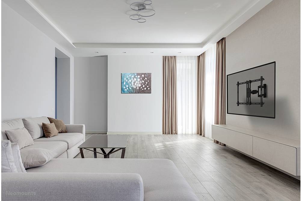 Helles Wohnzimmer mit modernen Möbeln: graues Sofa, Couchtisch, Wandkunst und leere Wandhalterung für TV. Holzboden und helle Vorhänge.