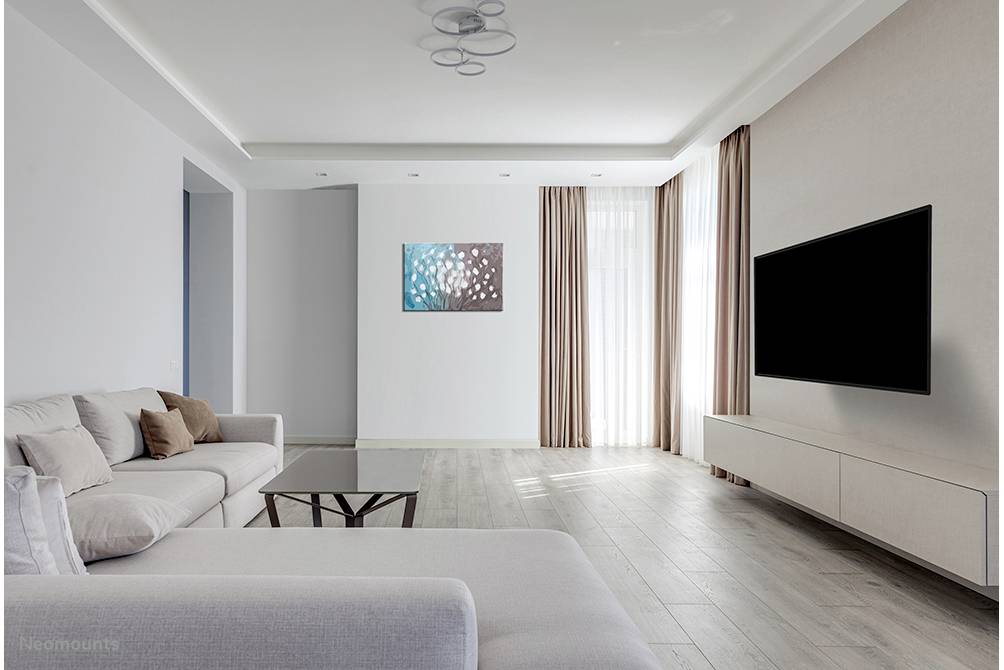 Modernes Wohnzimmer mit hellem Sofa, Couchtisch und großem Flachbildfernseher an der Wand. Bodentiefe Fenster mit Vorhängen.