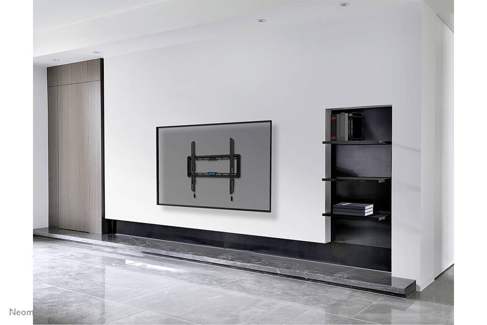 Ein moderner, minimalistisch eingerichteter Raum mit einem flach an der Wand angebrachten Fernseher und einem Regal mit Büchern.