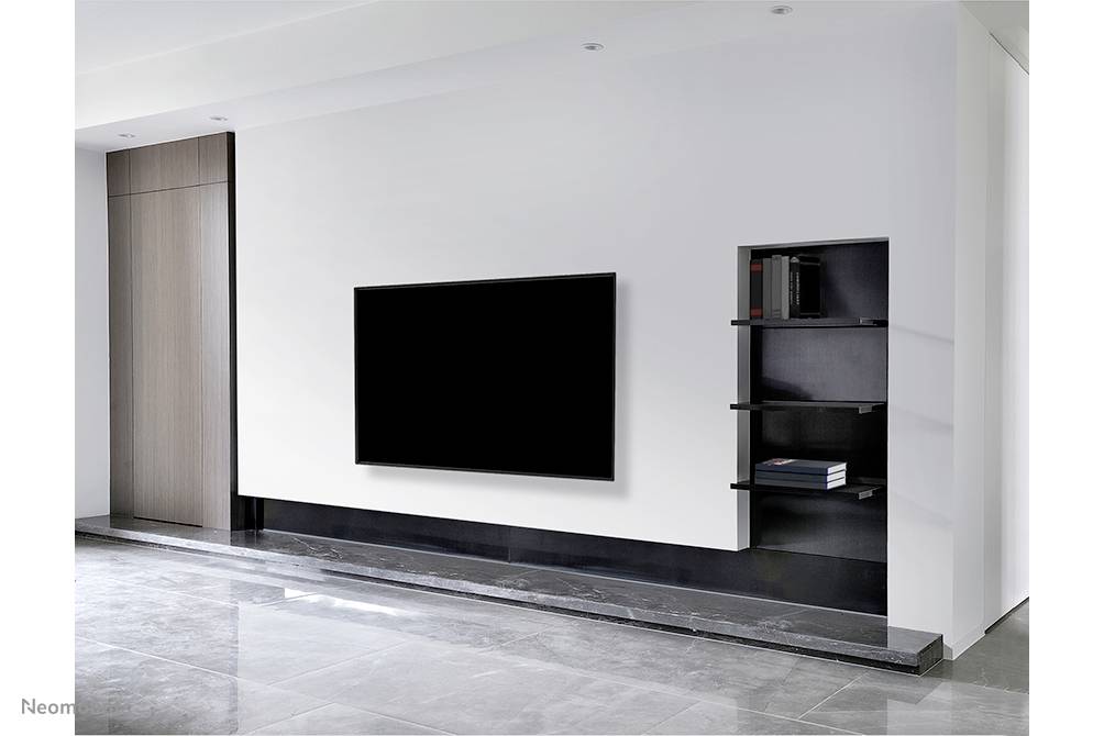 Ein Wohnzimmer mit einem großen, schwarzen Fernseher an der weißen Wand. Daneben schwimmende Regale mit Büchern und Dekorationen.