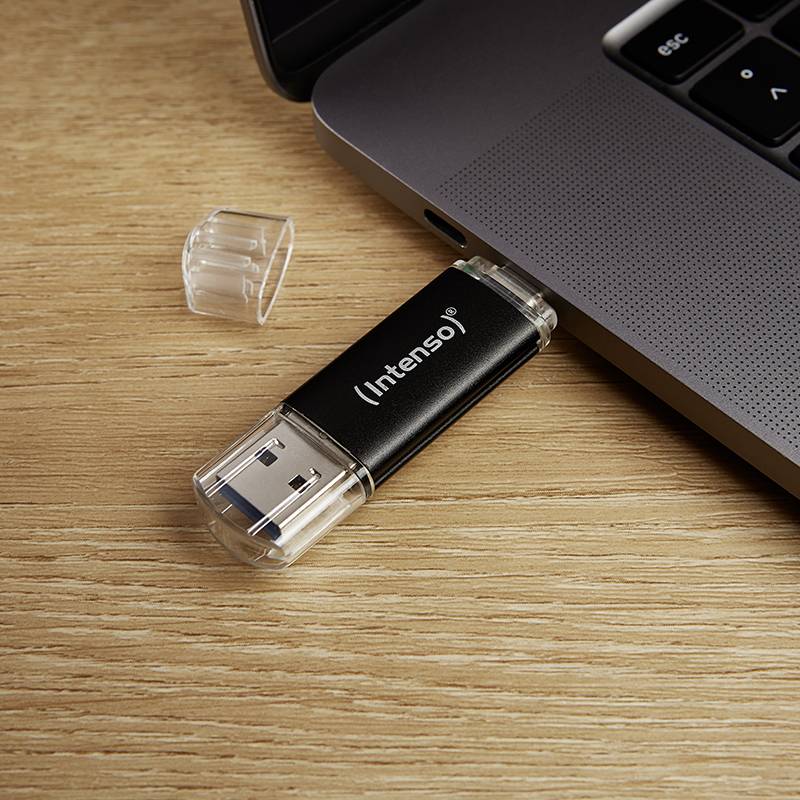 Ein schwarzer USB-Stick der Marke Intenso wird in einen Laptop auf einem Holztisch eingesteckt.