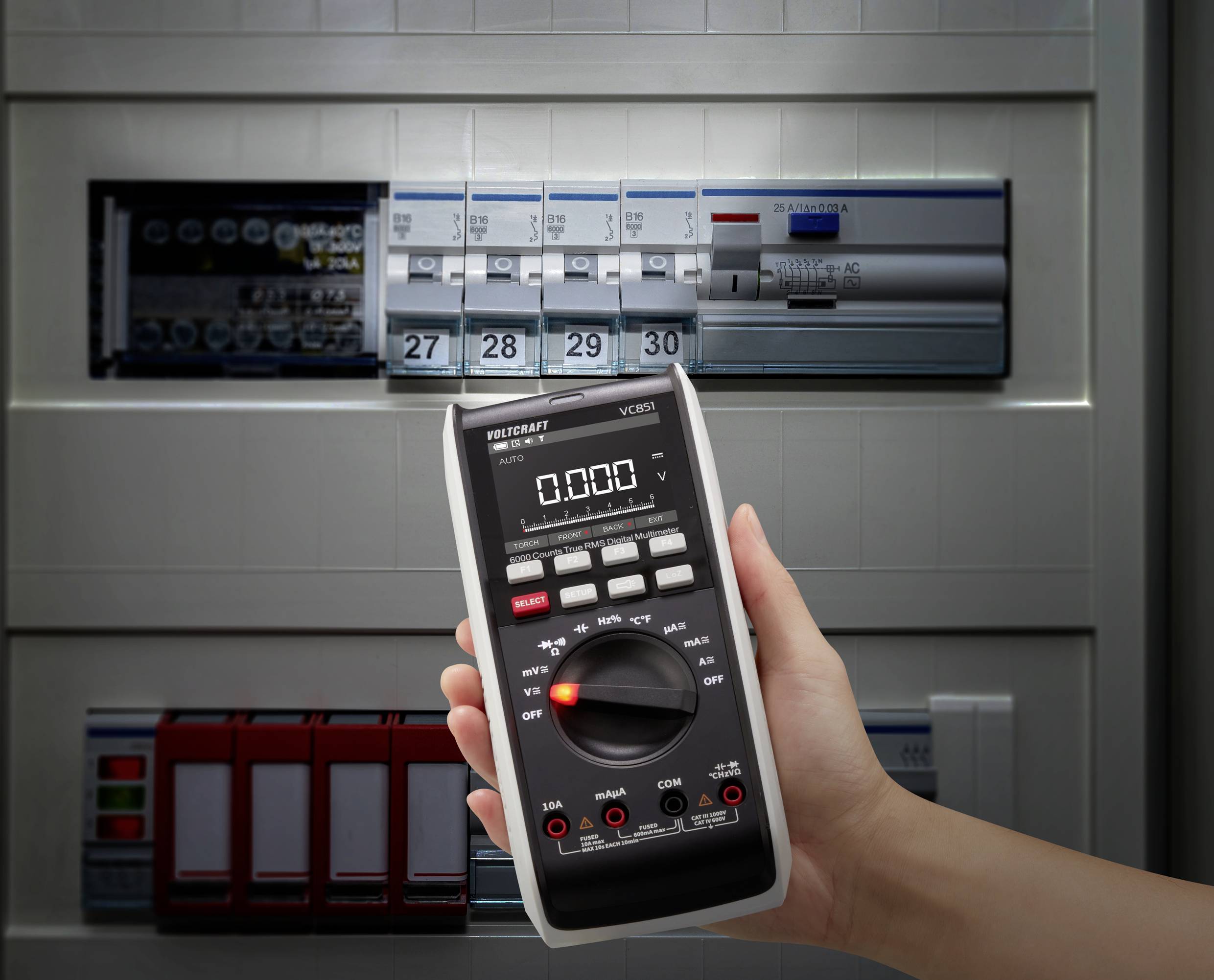 Hand hält ein Multimeter, zeigt 0.00, vor geöffnetem Stromkasten mit Schaltern und Sicherungen, symbolisiert elektrische Prüfung.