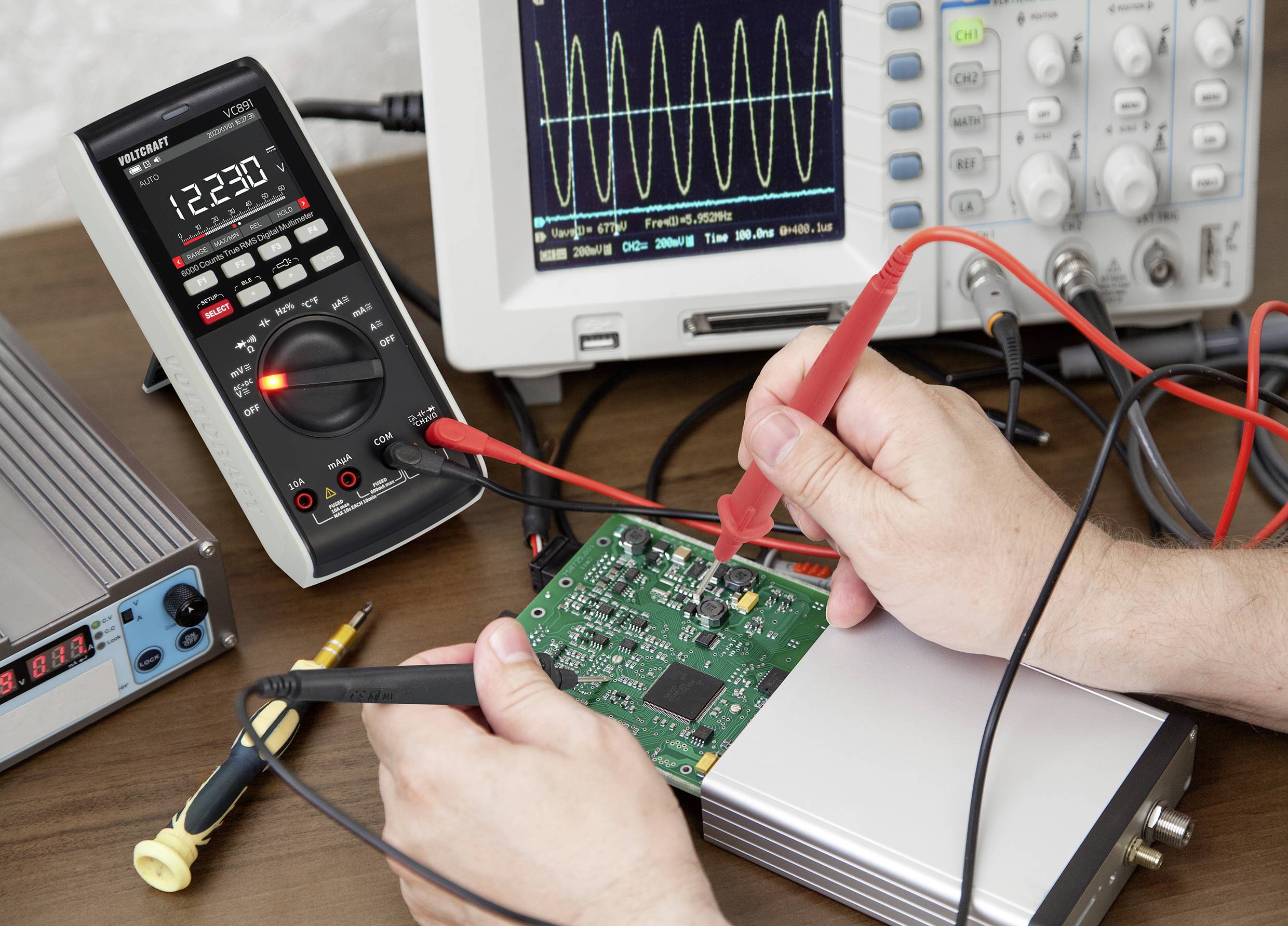 Eine Person testet eine grüne Leiterplatte mit einem Multimeter, während auf einem Oszilloskop eine Sinuswelle angezeigt wird.