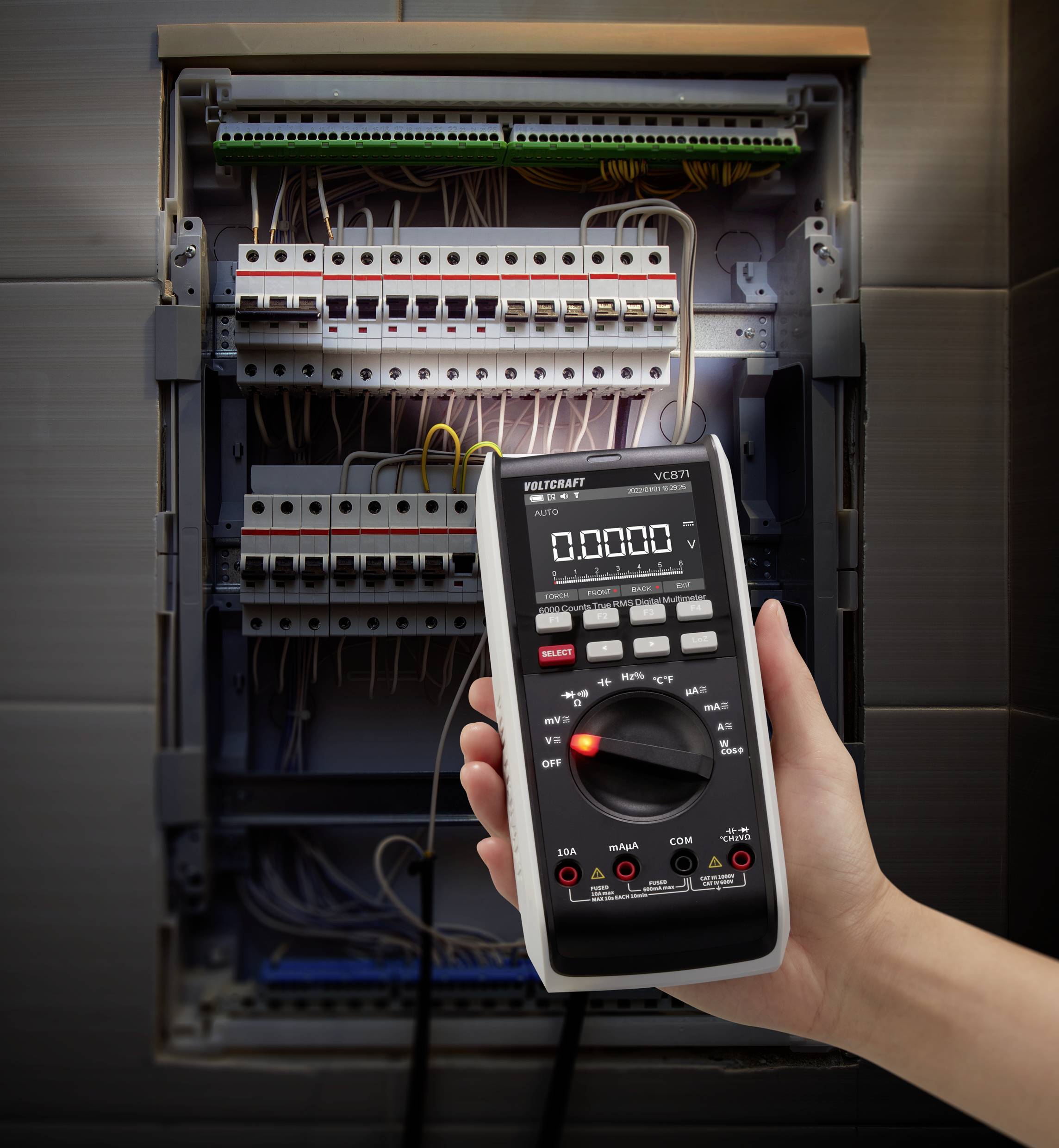Eine Hand hält ein digitales Multimeter vor einem geöffneten Stromverteilerkasten, um elektrische Werte zu messen.