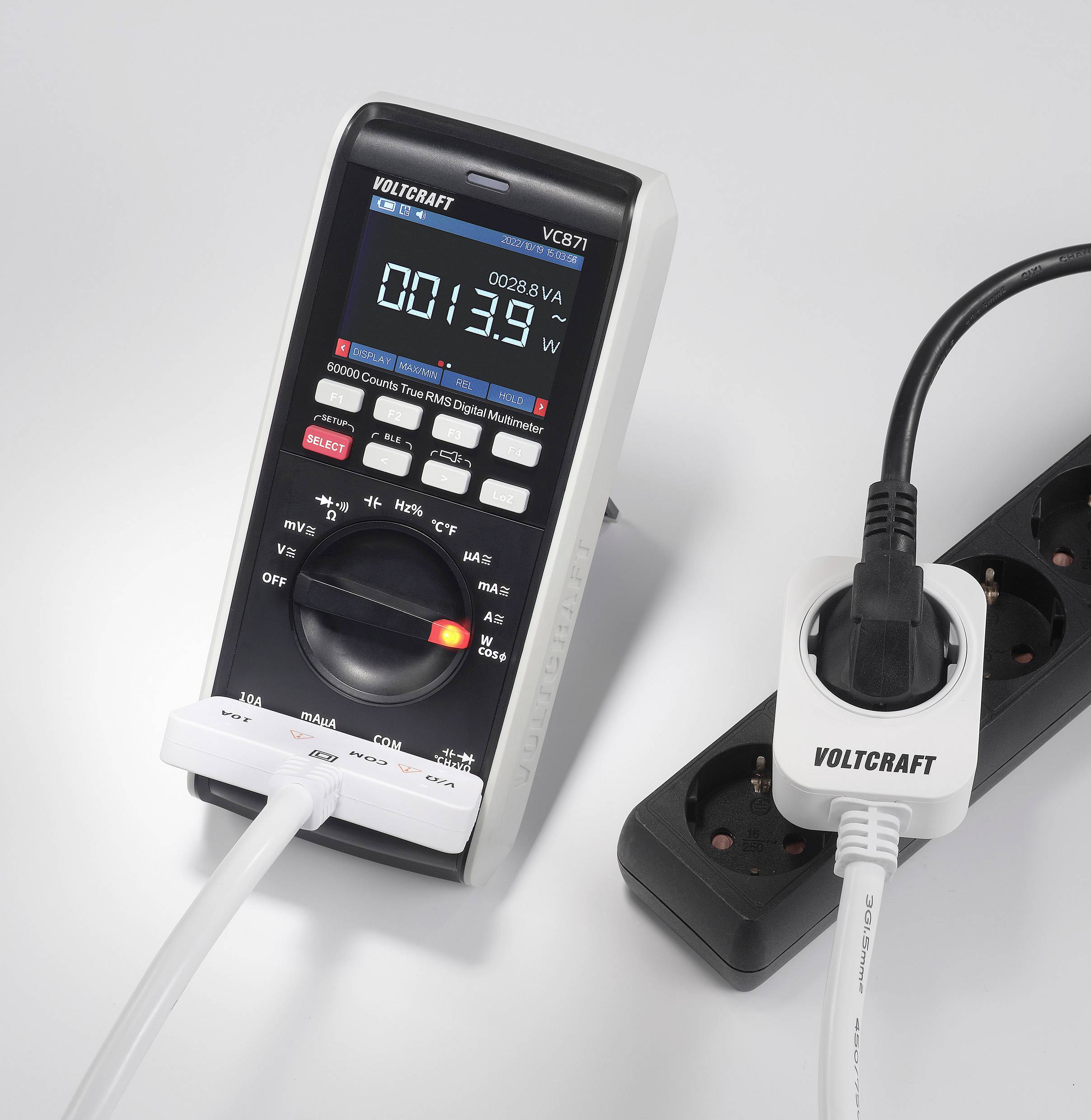 Ein digitales Multimeter misst Stromstärke, verbunden mit einem Verlängerungskabel, das in eine Steckdosenleiste eingesteckt ist.