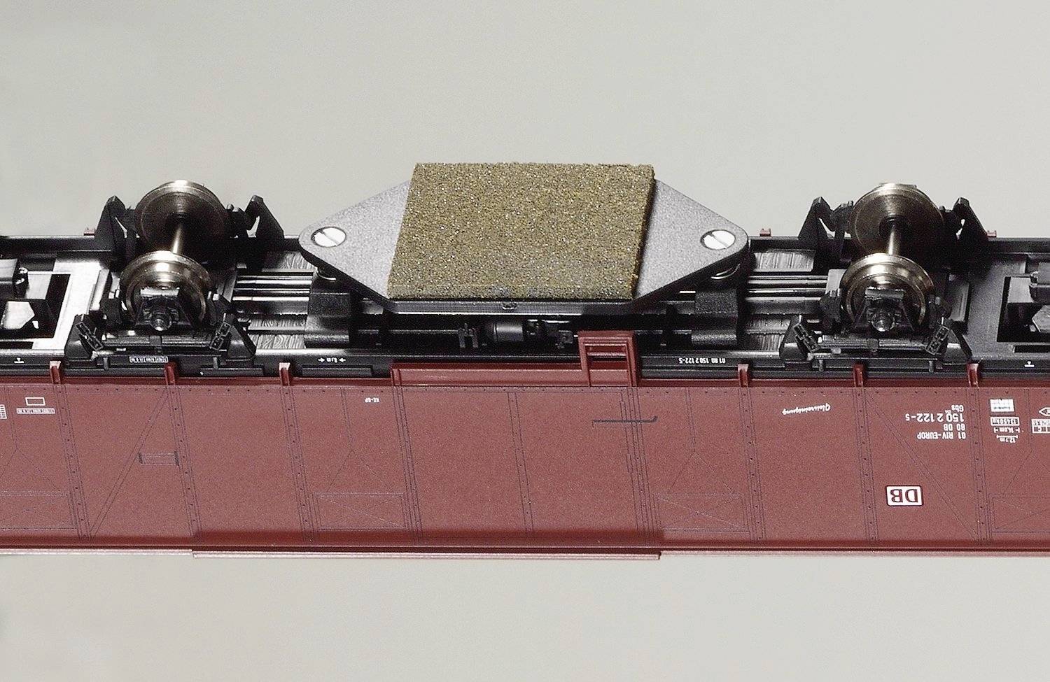 Ein Modell einer Zugunterseite mit einem Rostschutz-Pad in der Mitte, umgeben von Fahrgestellen mit Rädern. Die Oberfläche ist dunkelrot.