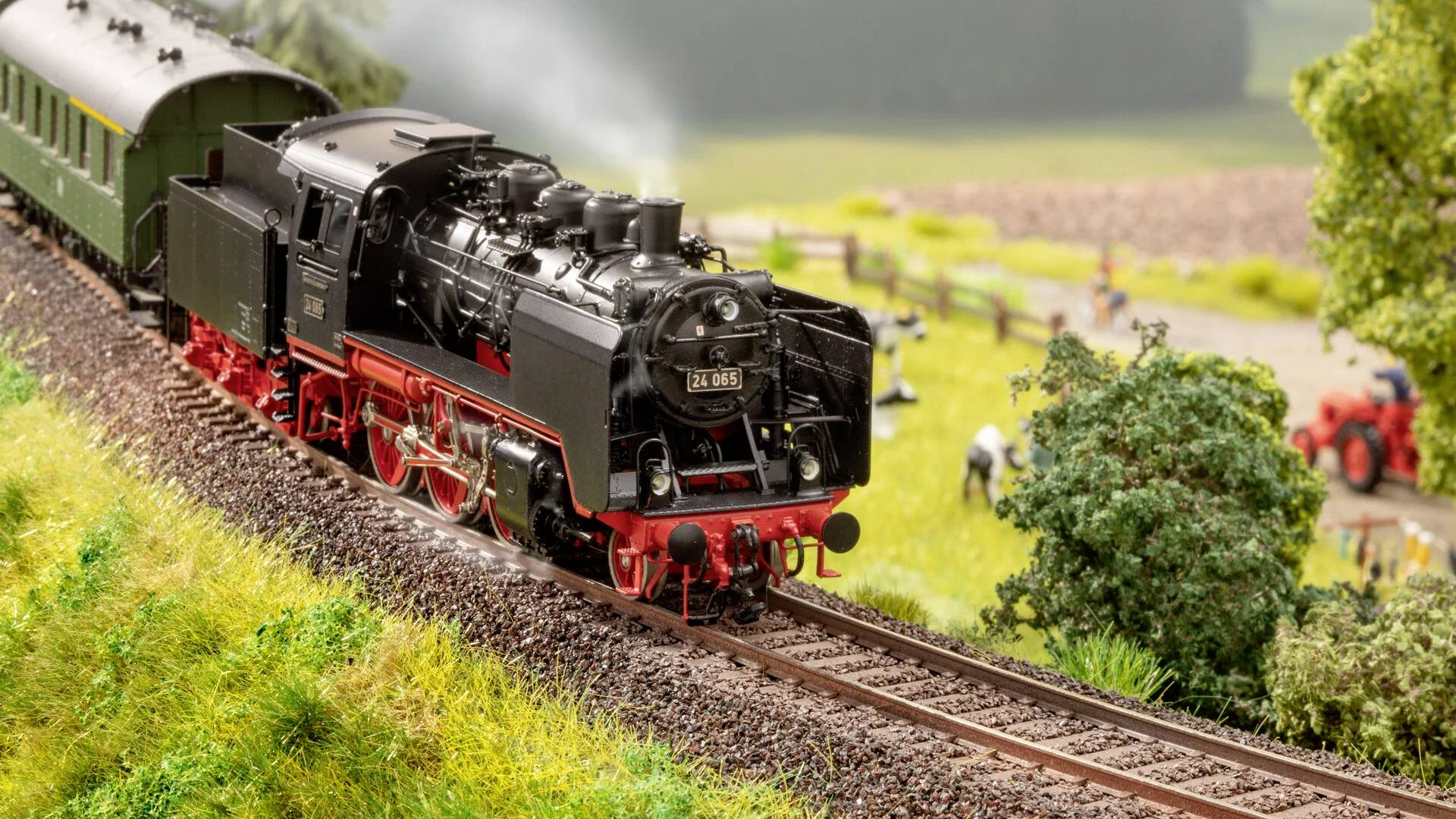 Eine schwarze Dampflokomotive fährt auf einer ländlichen Eisenbahnstrecke, umgeben von grüner Landschaft und einem vorbeiziehenden Zug.