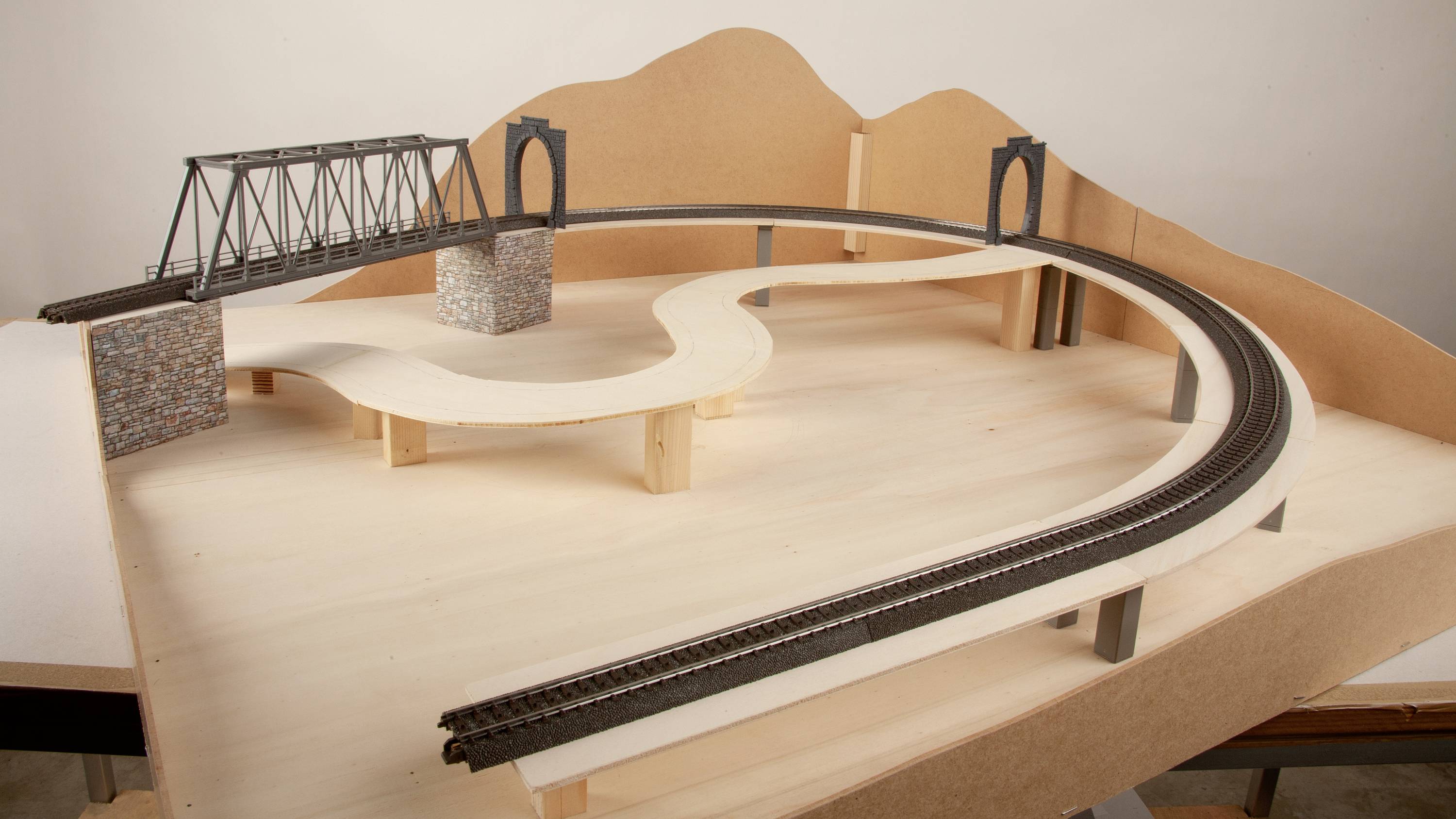 Modelleisenbahn-Landschaft im Aufbau mit Brücke und geschwungener Strecke, auf hölzerner Basis, ohne Dekorationselemente.