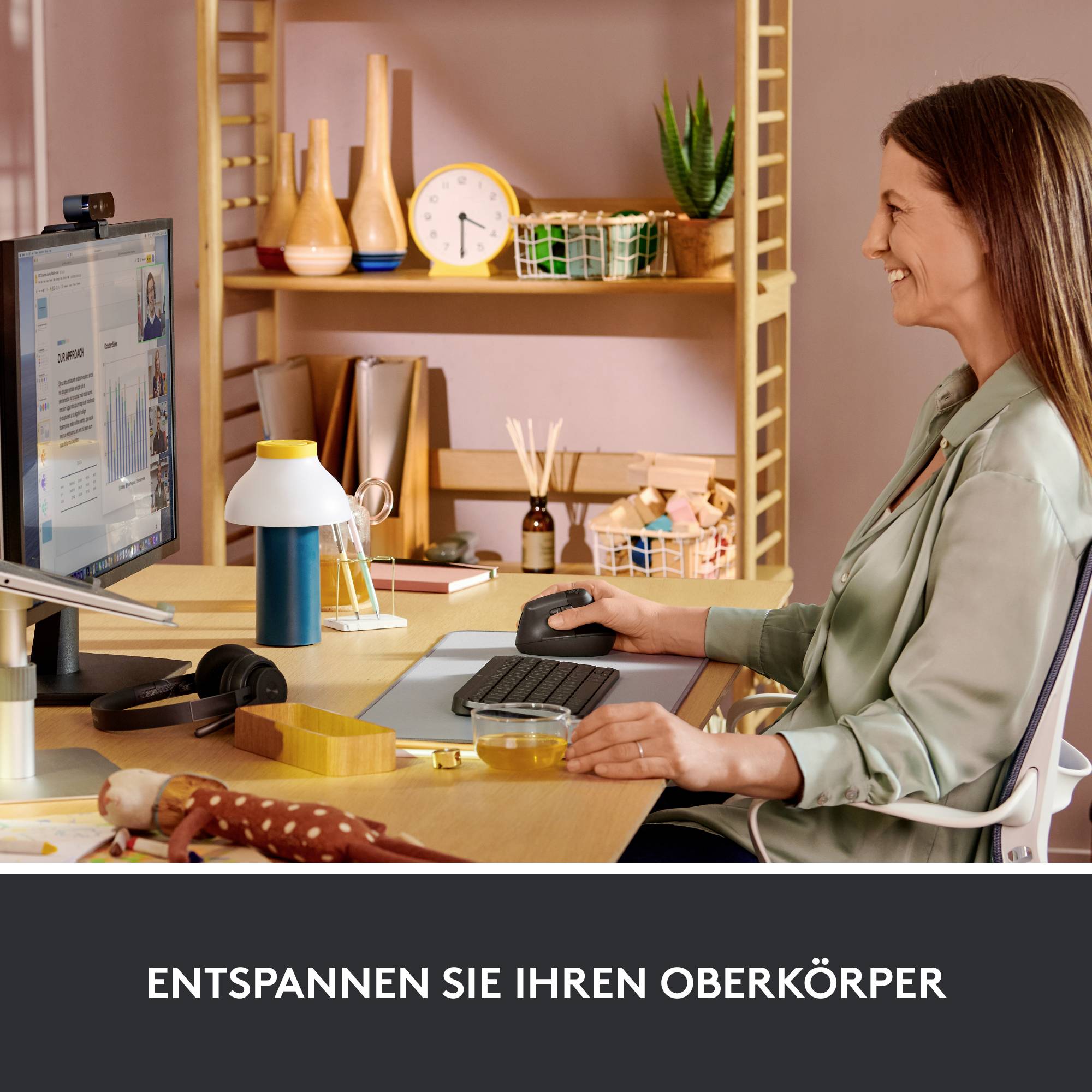 Eine Frau sitzt an einem Schreibtisch, entspannt den Oberkörper und betrachtet den Bildschirm. Im Hintergrund sind Regale mit Gegenständen.