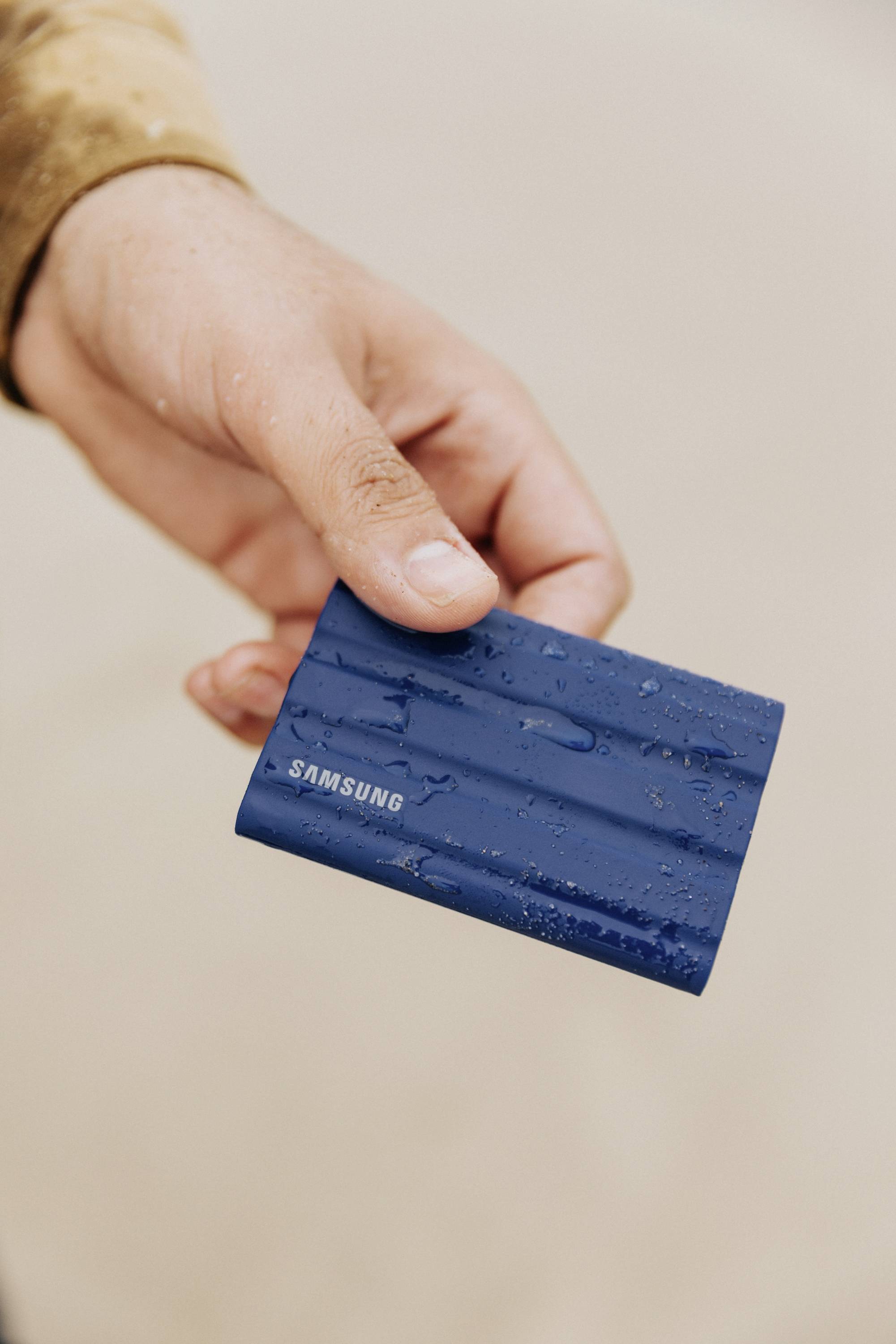 Eine Hand hält eine kleine, blaue Samsung-Festplatte, die mit Wassertropfen bedeckt ist.