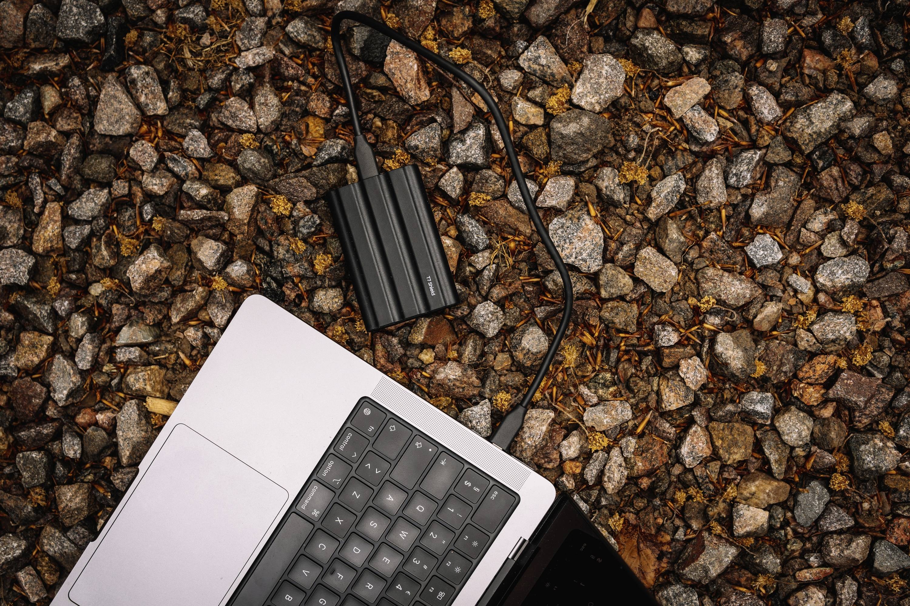 Ein Laptop liegt auf einem steinigen Untergrund, verbunden mit einem externen SSD-Laufwerk.