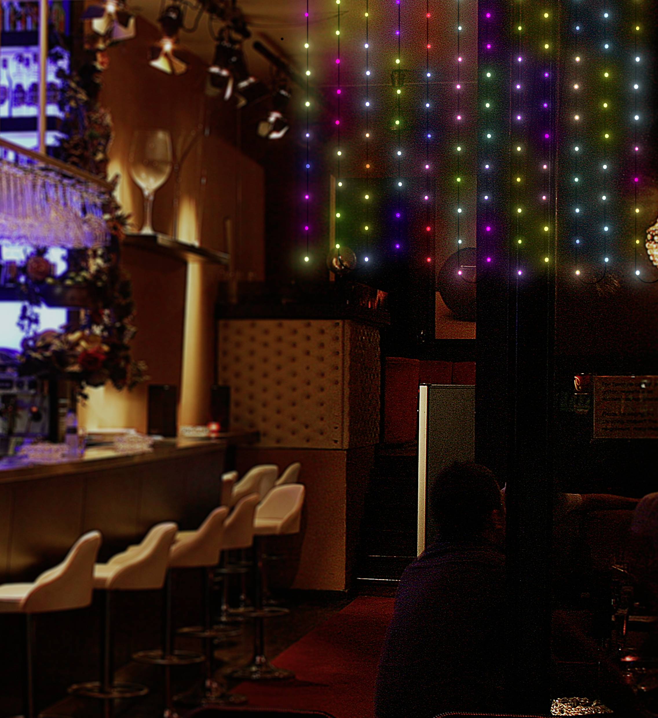 Eine stilvolle Bar mit leeren weißen Barhockern. Rechts leuchten bunte LED-Lichter an der Wand. Stimmungsvolle Beleuchtung.