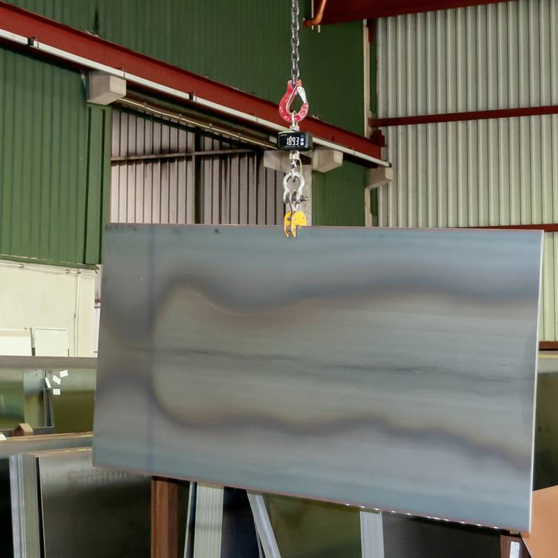 Stahlplatte wird in einer Werkhalle mit einem Kran transportiert. Die Umgebung zeigt industrielle Architektur und Lagerregale.