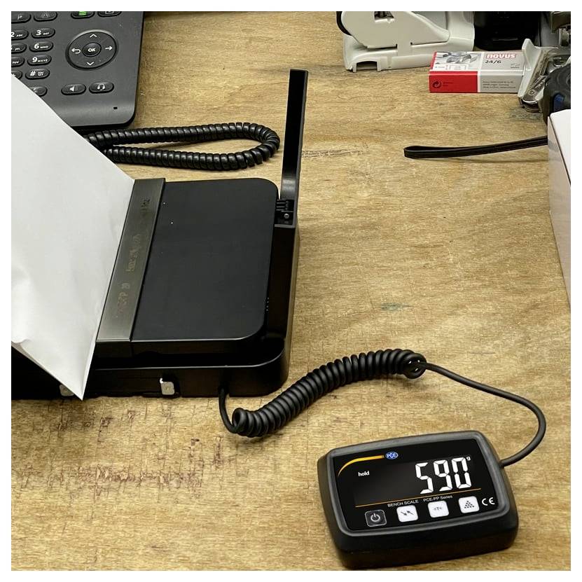Digitale Anzeige auf einem Drucker- oder Scanner-Setup zeigt 59,0 an, verbunden durch ein spiralförmiges Kabel auf einer Werkbank.