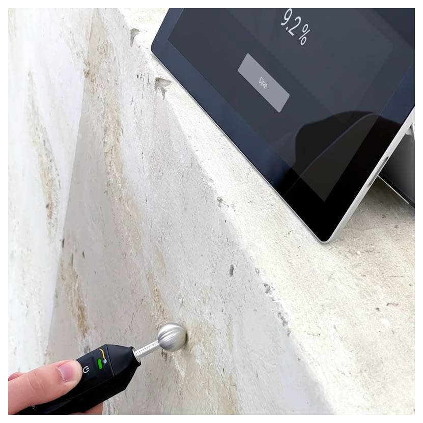 Ein tragbares Feuchtemessgerät testet eine Wand, während ein Tablet 92% Luftfeuchtigkeit anzeigt, was auf Nässe oder Wasserschäden hinweist.