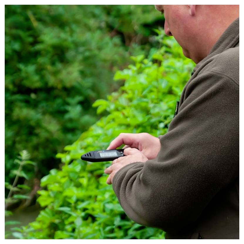 Mann im Freien in der Nähe von dichtem Grün, hält ein tragbares GPS- oder Telefongerät und benutzt es, während er darauf schaut.