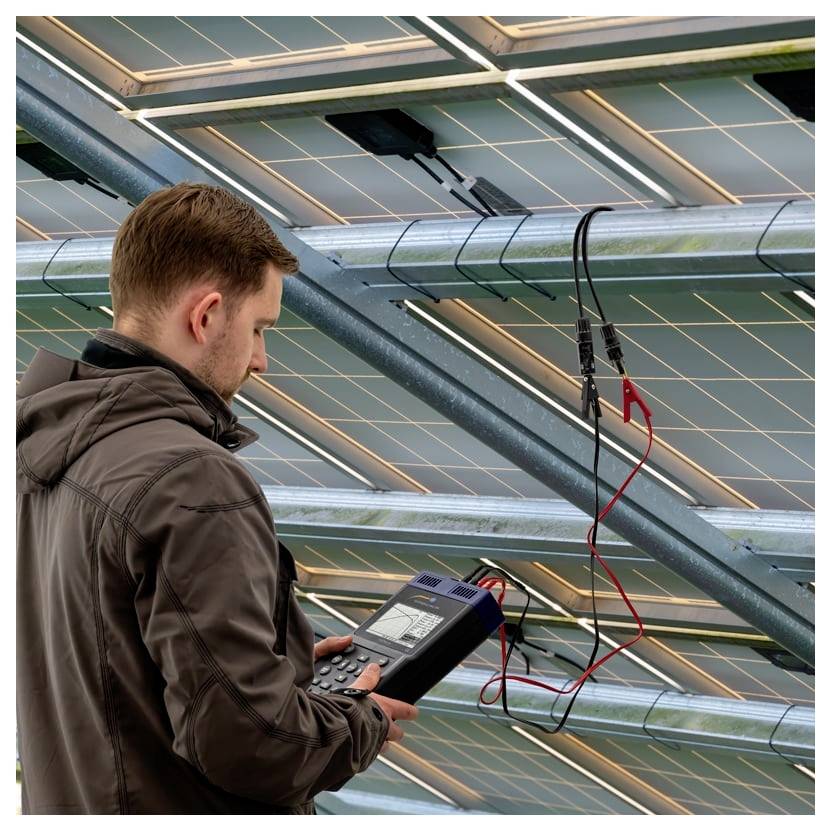 Techniker inspiziert Solarpanels mit einem tragbaren Messgerät und testet elektrische Anschlüsse auf einer Dachsolaranlage.
