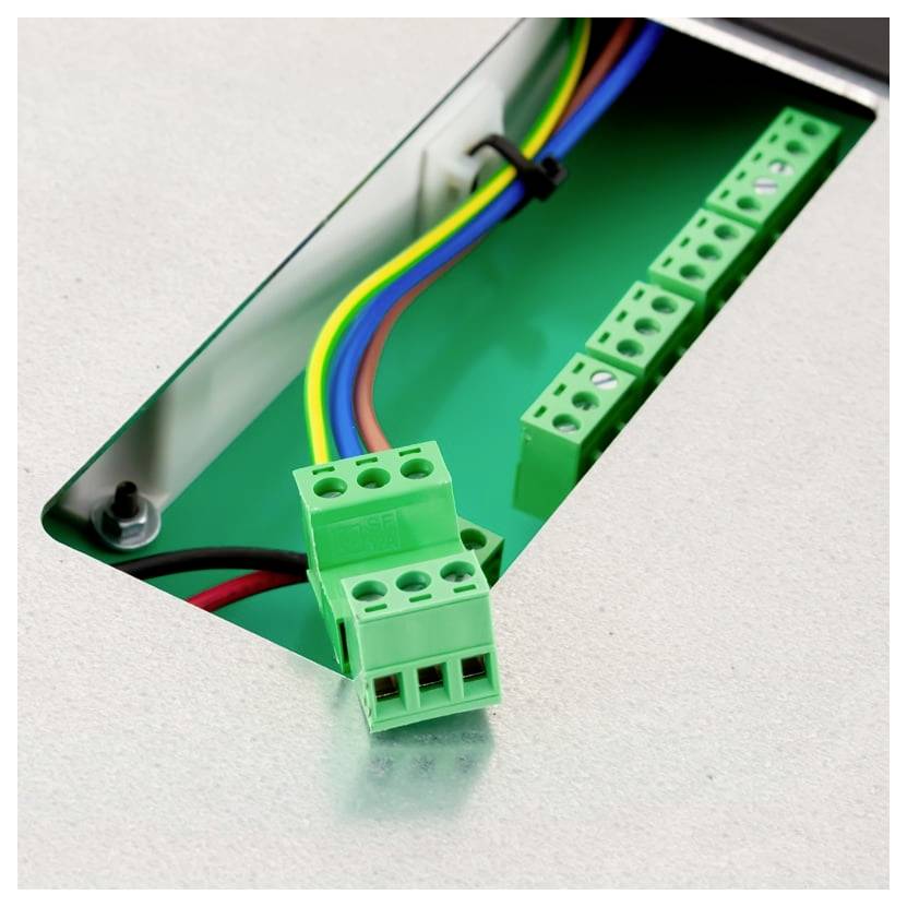Nahaufnahme einer elektrischen Klemmleiste mit mehrfarbigen Drähten, die durch eine Metallpanelöffnung verbunden sind.