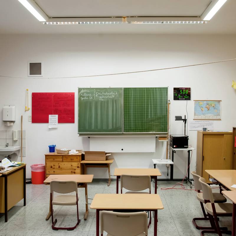 Leeres Klassenzimmer mit Tafel, Tischen und Stühlen. Eine Weltkarte und Uhr an der Wand.
