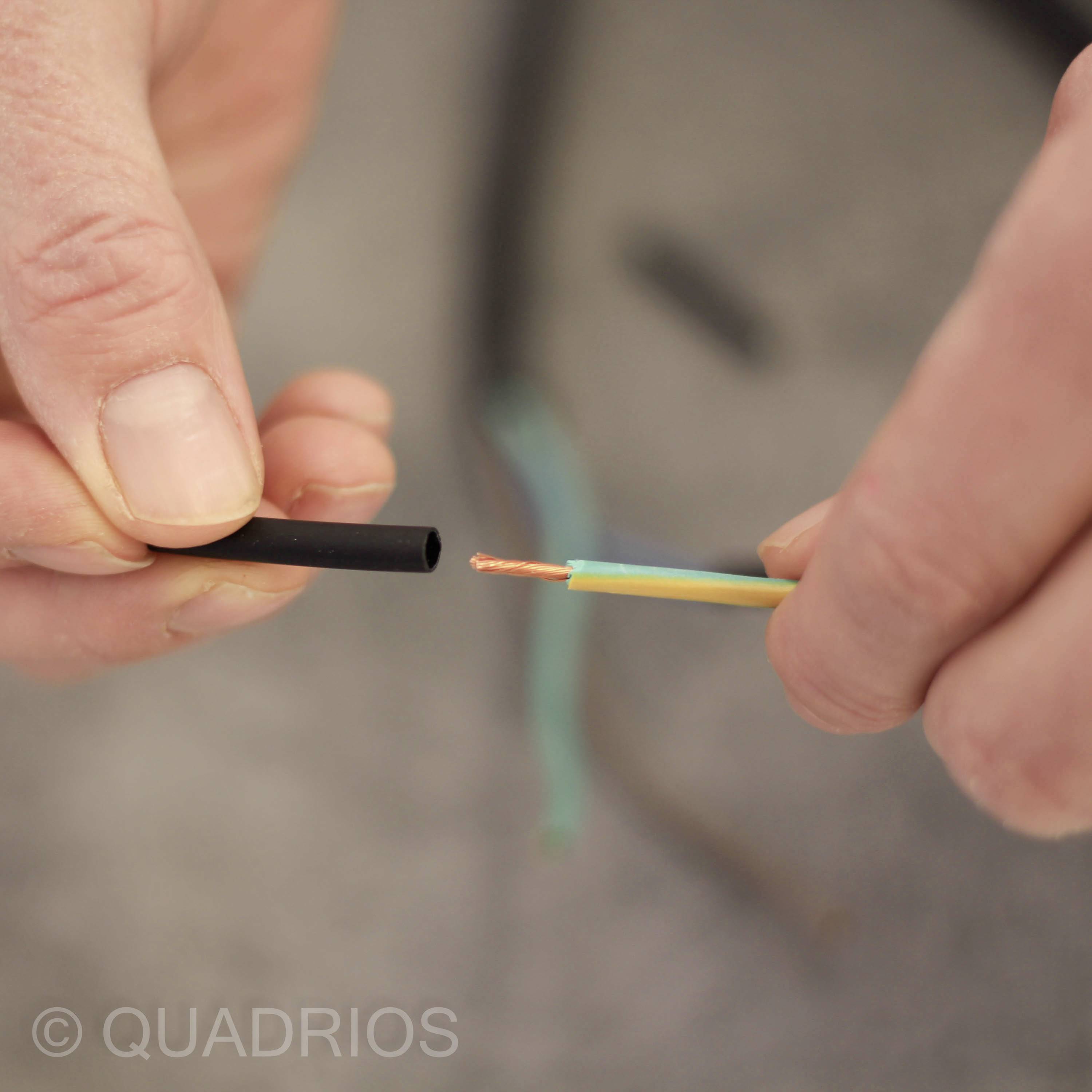 Eine Hand hält ein abisoliertes Kabel, das Drahtkern zeigt; eine andere Hand hält das Kabelisolationsstück.