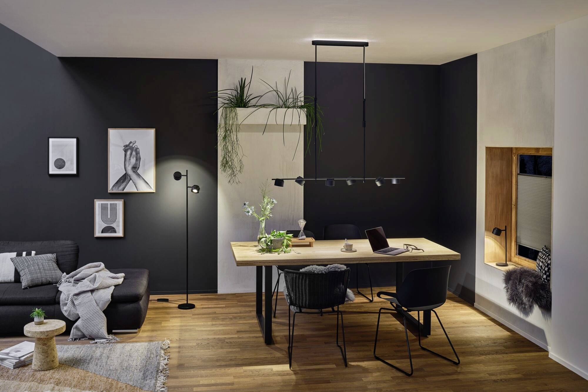 Ein modern eingerichtetes Wohnzimmer mit Esstisch, vier Stühlen und Pflanzen. Dunkle Wände und minimalistische Dekoration sind sichtbar.