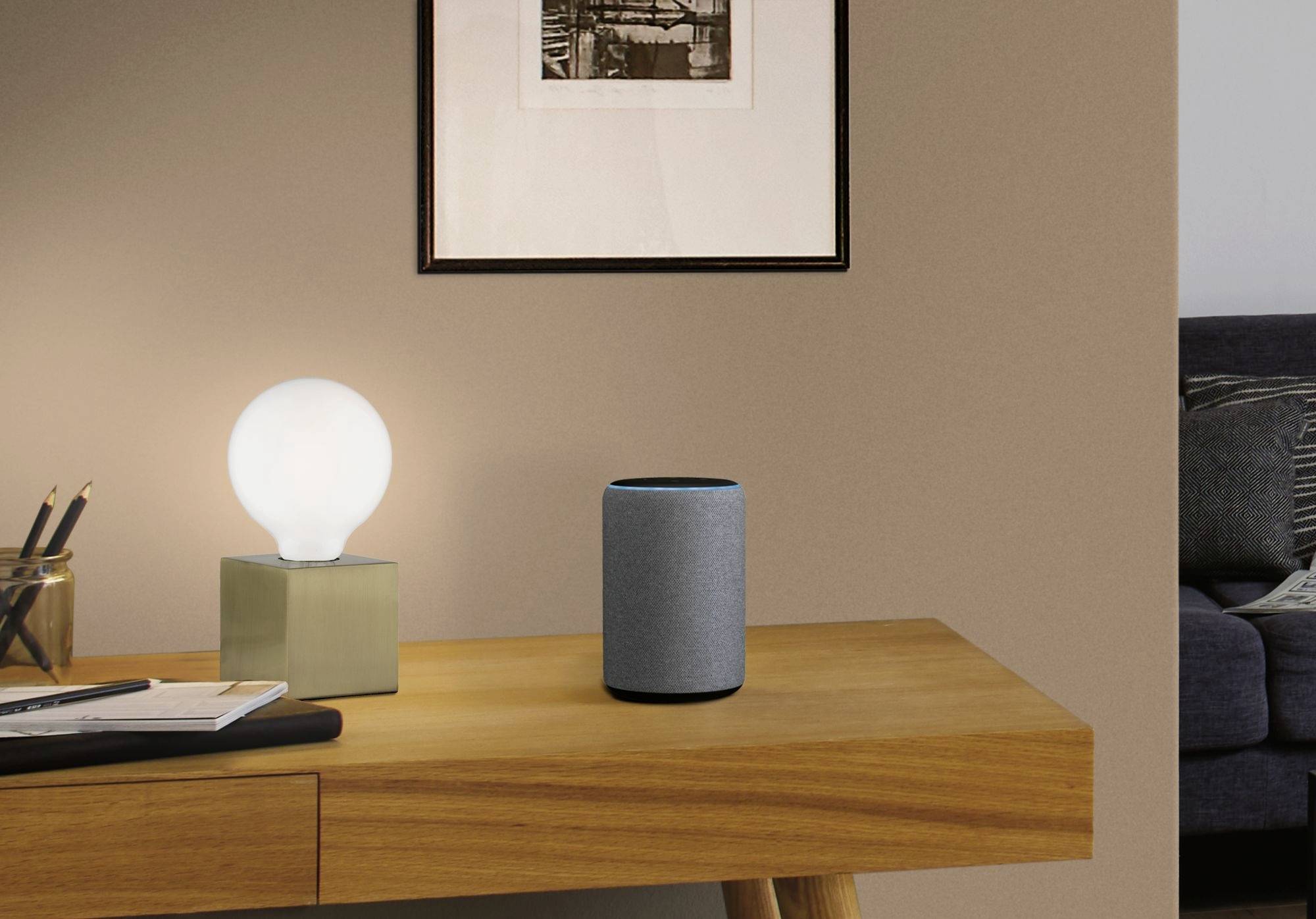 Holztisch mit einer Lampe und einem smarten Lautsprecher. An der Wand ein gerahmtes Bild. Teilweise sichtbares Sofa im Hintergrund.