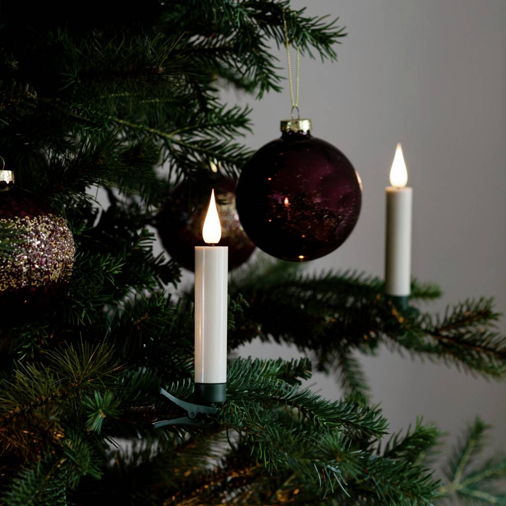 Ein Weihnachtsbaum mit Kugeln in dunklem Rot und weißen Kerzen. Die Kerzen leuchten sanft und schaffen eine festliche Atmosphäre.