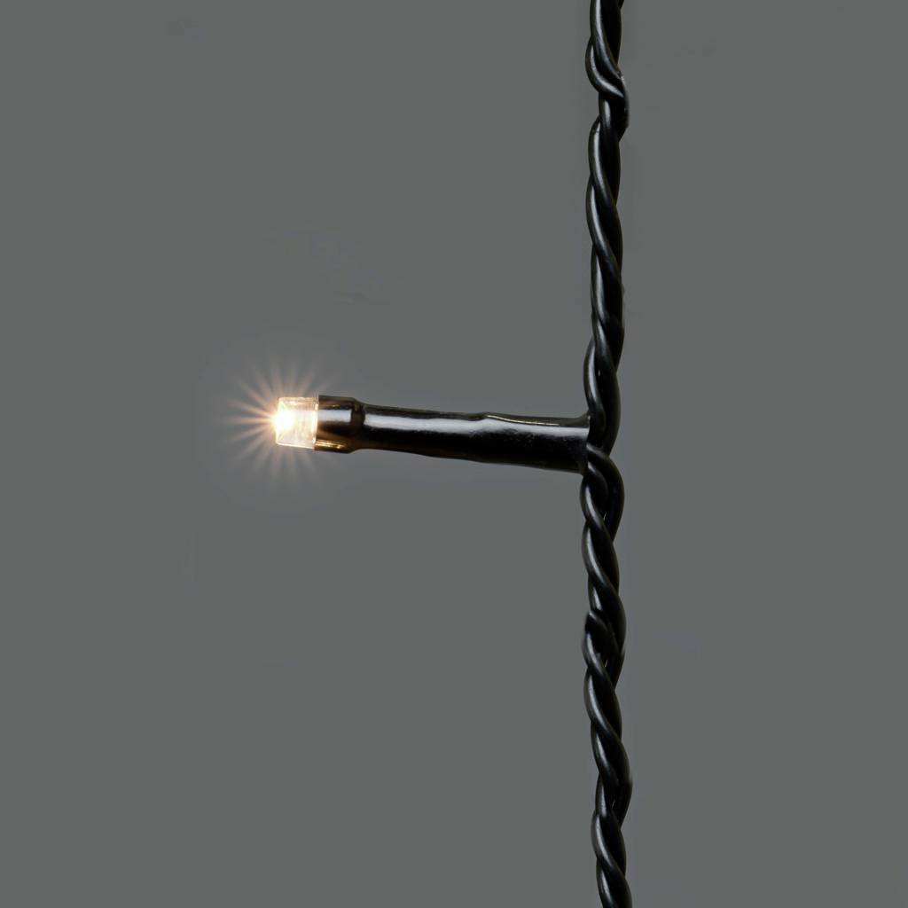 Nahaufnahme einer einzelnen, leuchtenden LED-Lampe an einer dunklen, verdrillten Lichterkette.