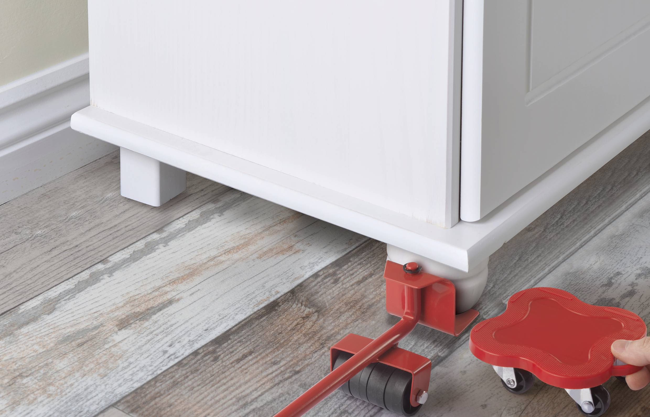 Eine Person bewegt ein Möbelstück mit einem roten Möbellift über einen Holzfußboden.