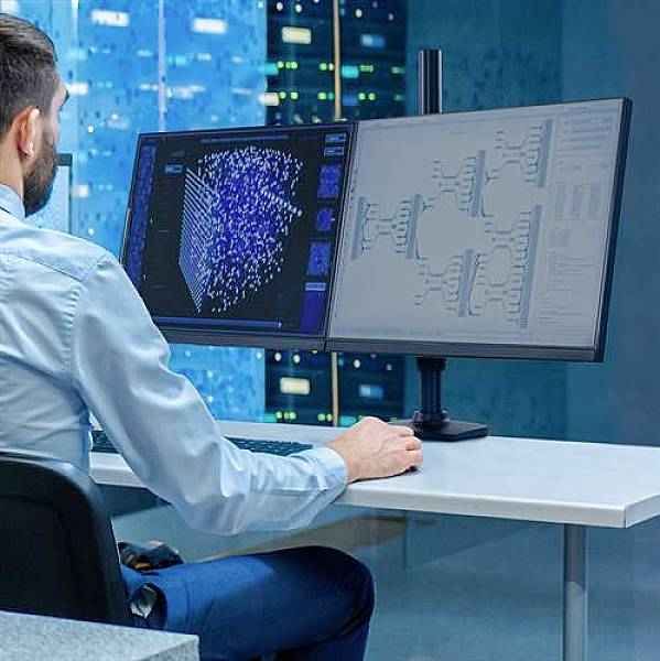 Eine Person arbeitet am Computer mit zwei Bildschirmen und analysiert Daten vor einem Hintergrund mit Servern.