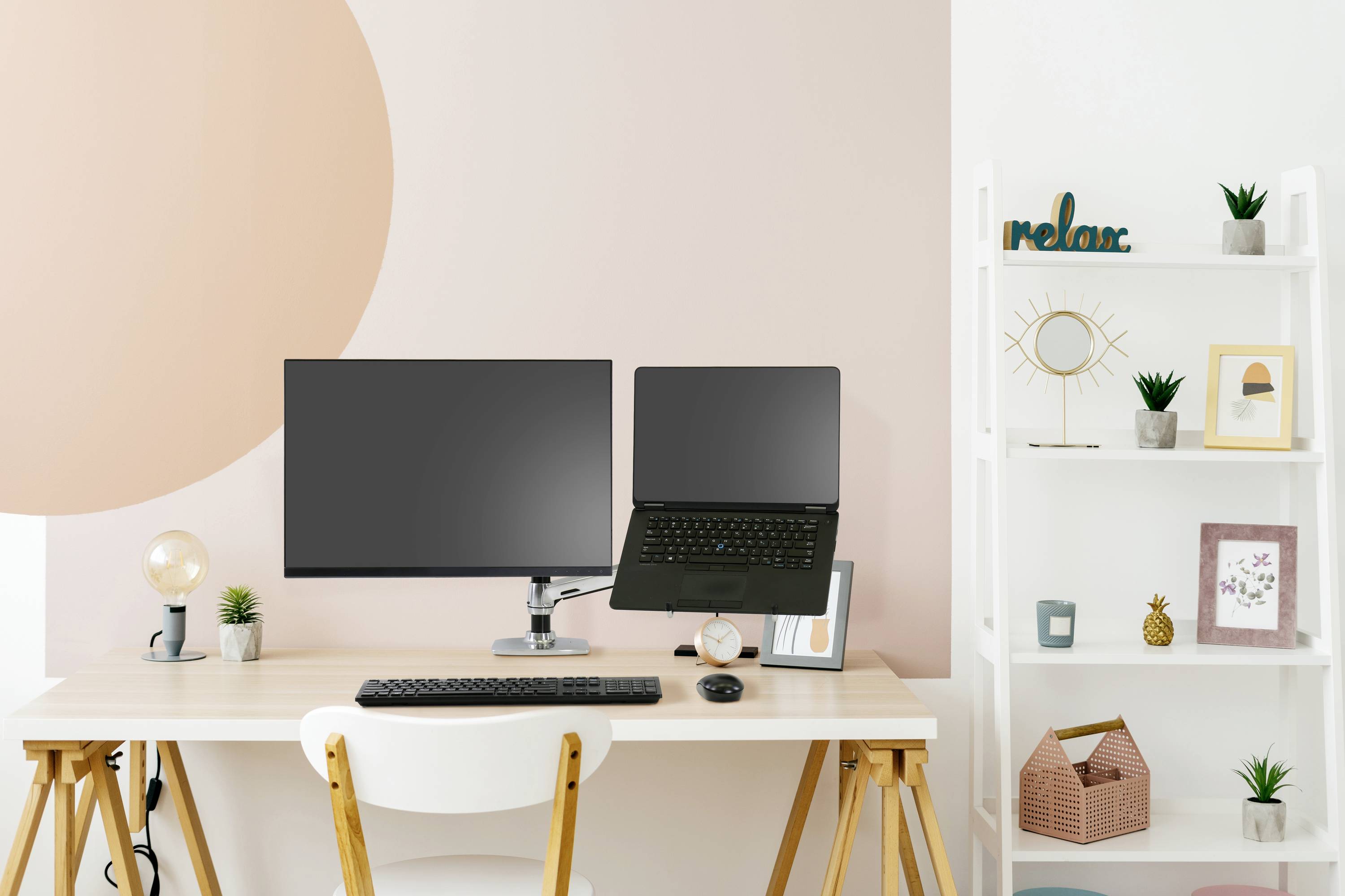 Ein moderner Schreibtisch mit einem Monitor, einem Laptop, einer Tastatur und einer Maus. Dekoration und Pflanzen auf einem weißen Regal.