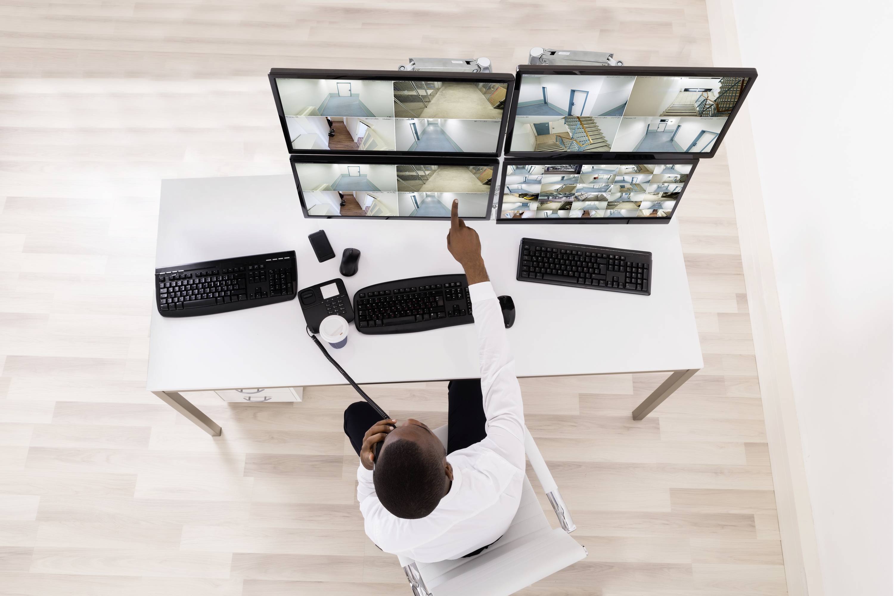 Eine Person überwacht mehrere Überwachungskameras auf Bildschirmen in einem Büro. Sie benutzt ein Walkie-Talkie.