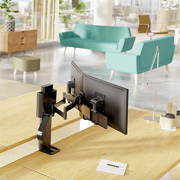 Arbeitsbereich mit zwei modernen Monitoren auf einem Tisch, Blick auf ein stilvoll eingerichtetes Büro mit Sofas im Hintergrund.