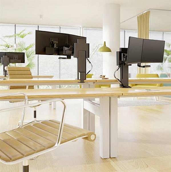 Büro mit modernen Schreibtischen und Monitorarmen, leeren Stühlen und großen Fenstern, die viel Tageslicht hereinlassen.