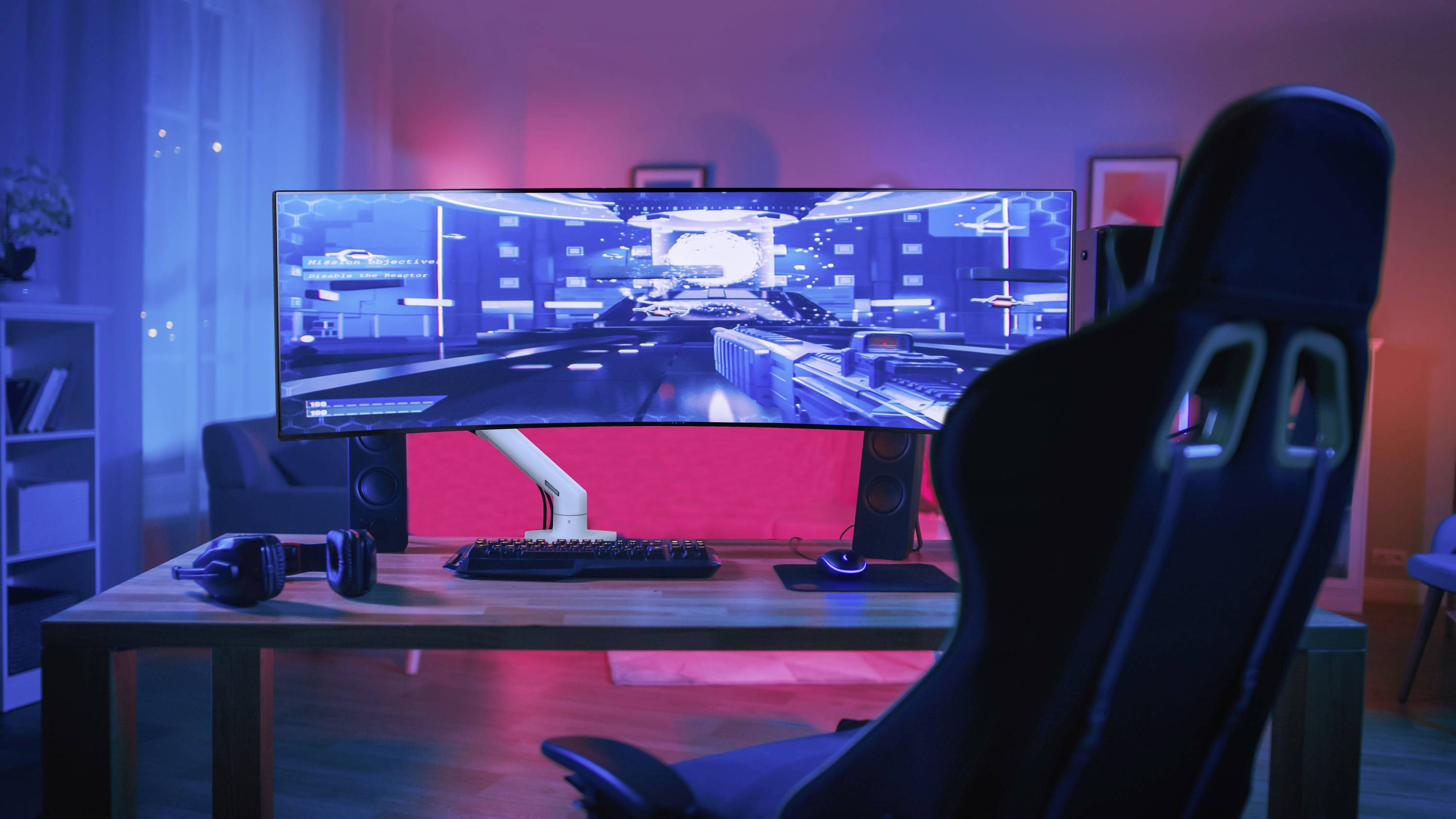 Ein Computer-Schreibtisch mit einem großen, gebogenen Monitor zeigt ein Videospiel. Ein Gaming-Stuhl steht davor in einem rot-blau beleuchteten Raum.