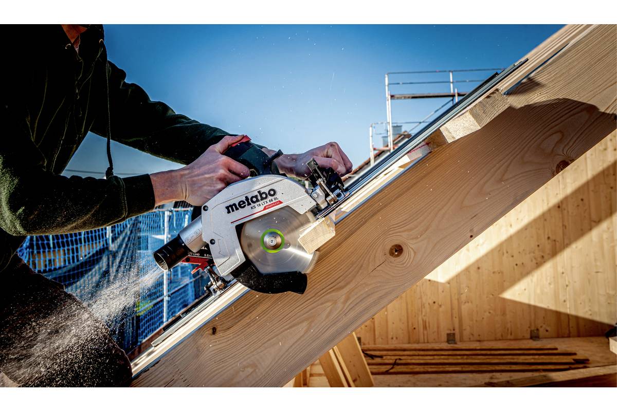 Eine Person sägt mit einer Kreissäge ein Holzbrett auf einer Baustelle. Die Kreissäge trägt die Aufschrift 'metabo'.