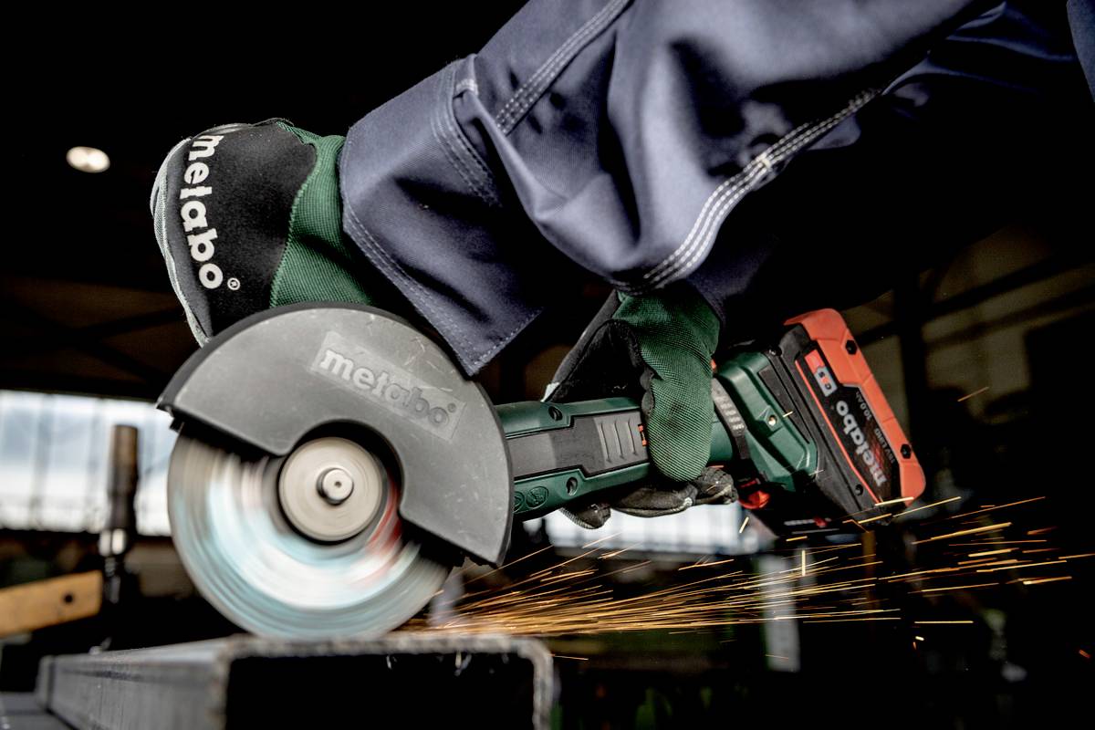 Ein Arbeiter benutzt einen Winkelschleifer, um ein Metallelement zu schneiden. Funken sprühen dabei in einer Werkhalle.
