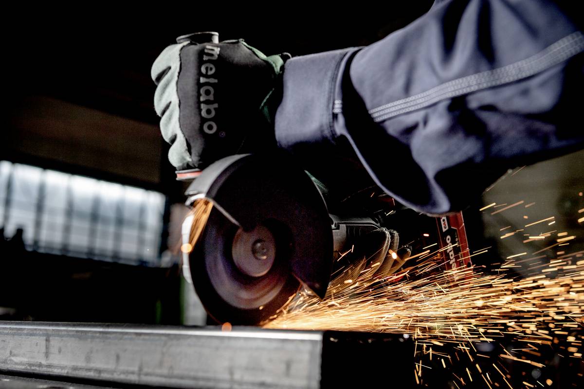Arbeiter mit Schutzhandschuhen schleift ein Metallstück, Funken fliegen.