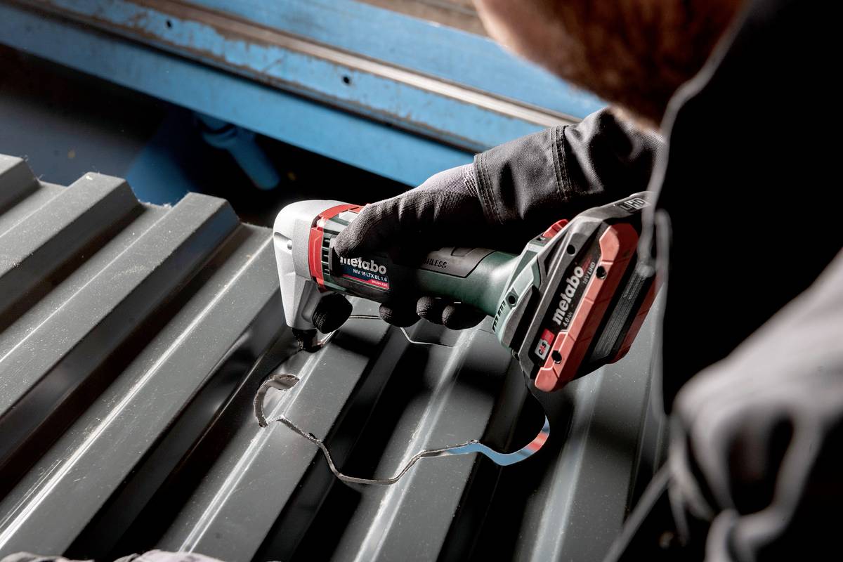 Person schneidet mit einem Metabo Elektrowerkzeug ein Wellblech, umgeben von metallischer Umgebung.