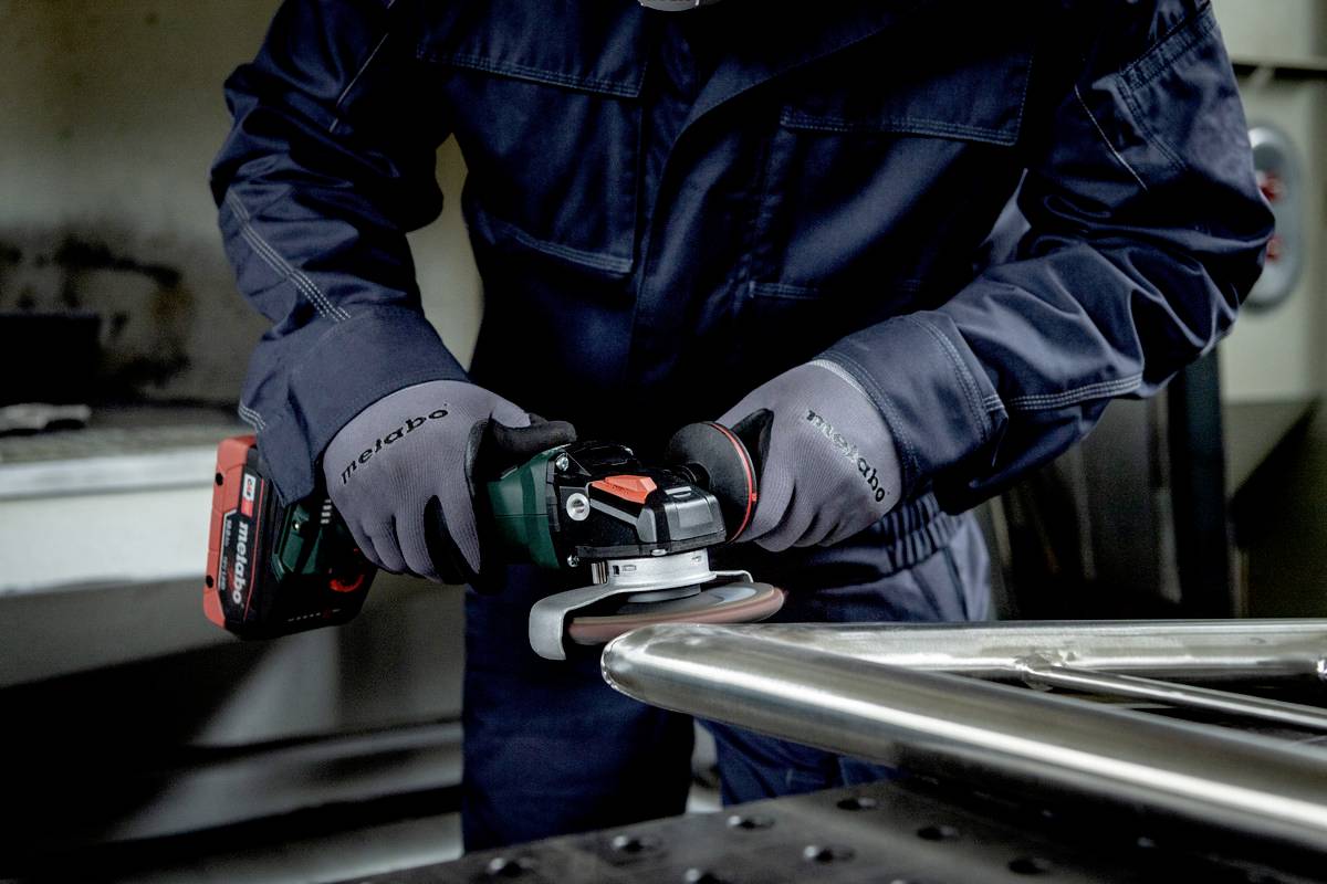 Person in Schutzkleidung schleift Metall mit einem elektrischen Schleifgerät.