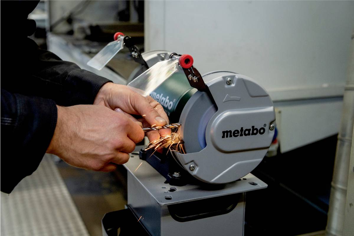 Eine Person schleift einen Metallgegenstand an einer Metallschleifmaschine, Funken sprühen. Maschinenteil mit 