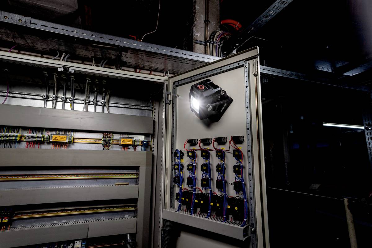 Ein geöffneter Schaltschrank mit mehreren Sicherungen und Kabelsträngen, beleuchtet von einer angebrachten Lampe, in einer industriellen Umgebung.