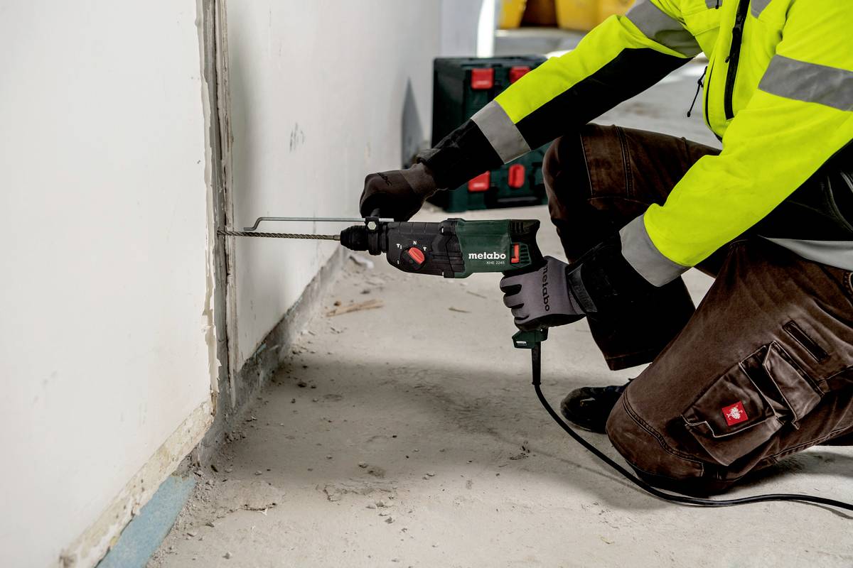 Eine Person in Sicherheitskleidung verwendet eine elektrische Säge, um einen Schlitz in eine weiße Wand zu schneiden.