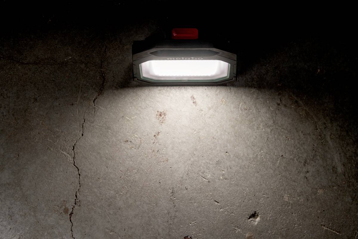 Tragbare Lampe wirft Licht auf dunklen Betonboden. Ein roter Schalter ist auf der Lampe sichtbar.