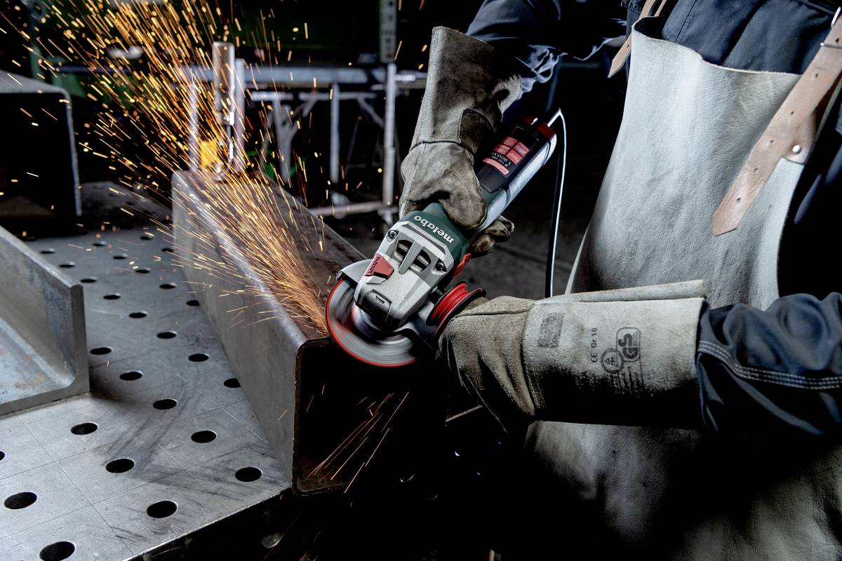 Eine Person schleift ein Metallstück mit einem Winkelschleifer. Funken fliegen, während die Arbeitsfläche aus Metall besteht.