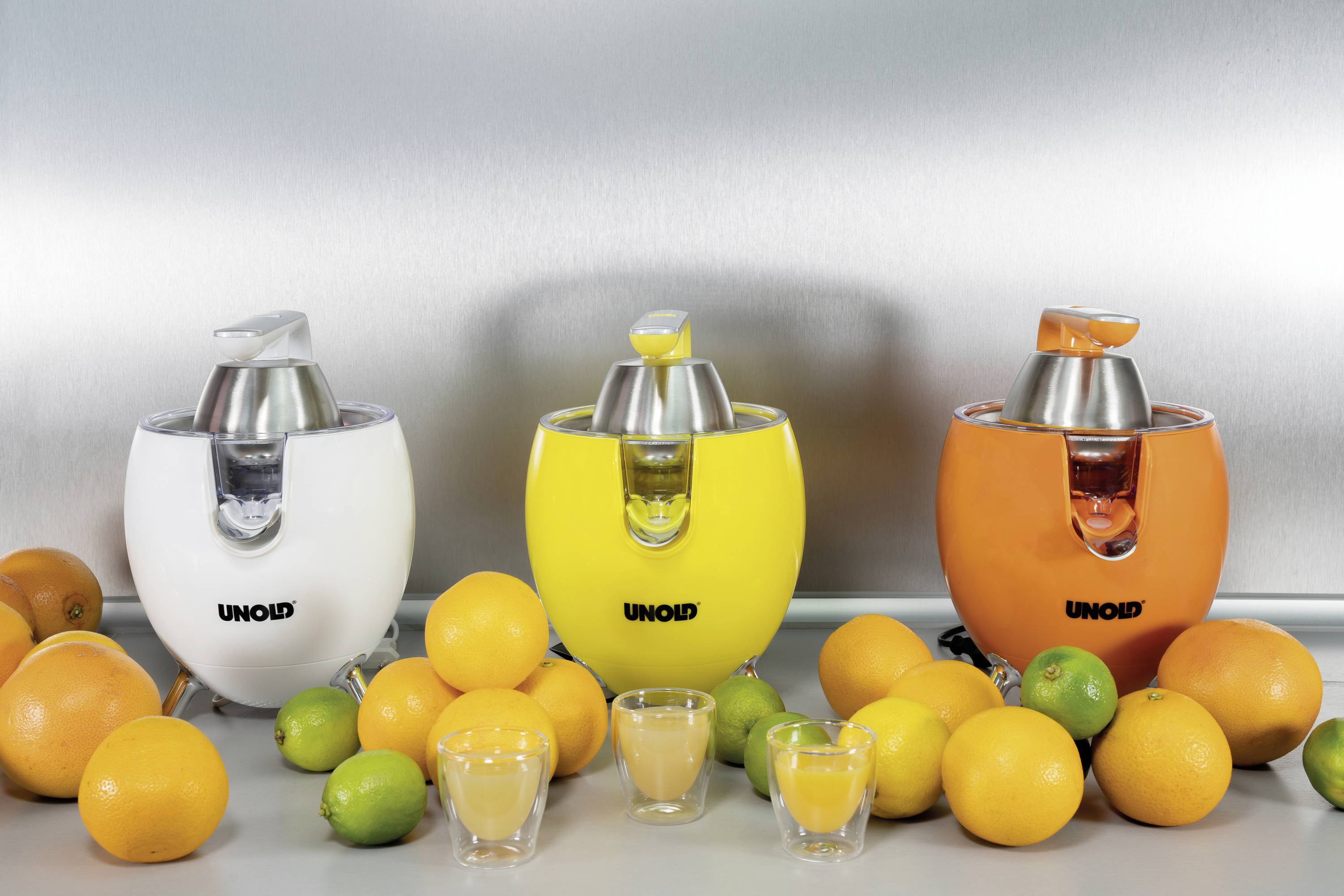 Drei elektrische Entsafter in Weiß, Gelb und Orange stehen nebeneinander, umgeben von Orangen und Limetten. Gläser mit Saft davor.